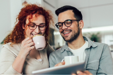 An iamge of a woman and a man drinking coffee as they both look at a tablet