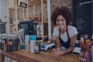 An image of a young woman leaning on a checkout counter with various food items around her. The image also has an illustrated label that says, Coming to Hello Alice Spring 2023.