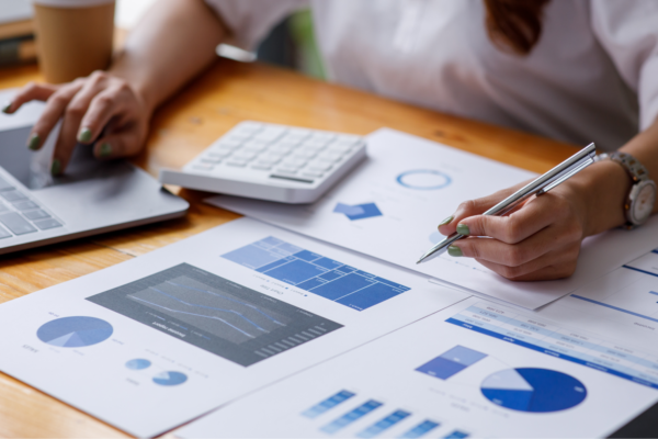 A person works on a computer with a calculator and financial documents on the desk in front of them.