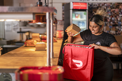 An image of a young woman at a restaurant putting food into a DoorDash bag