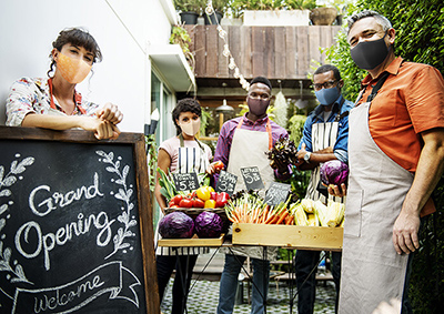 A group of men and women standing in front of a table with fresh veggies on it